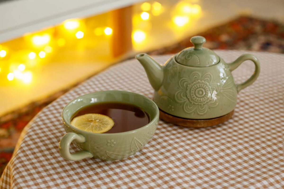 Services Green ceramic teapot and lemon-infused tea in a cozy indoor setting with warm lights.